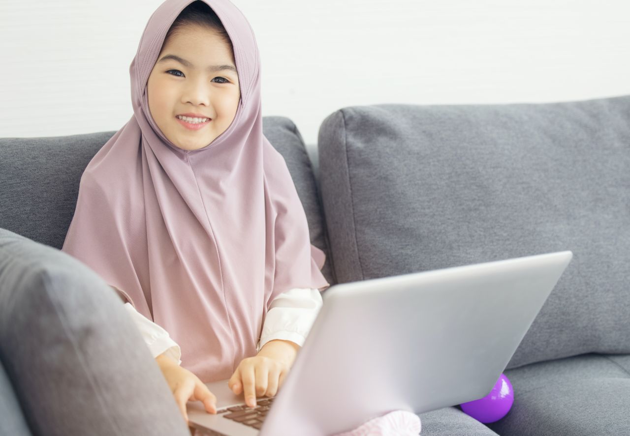 Young girl sitting on a couch with a laptop.